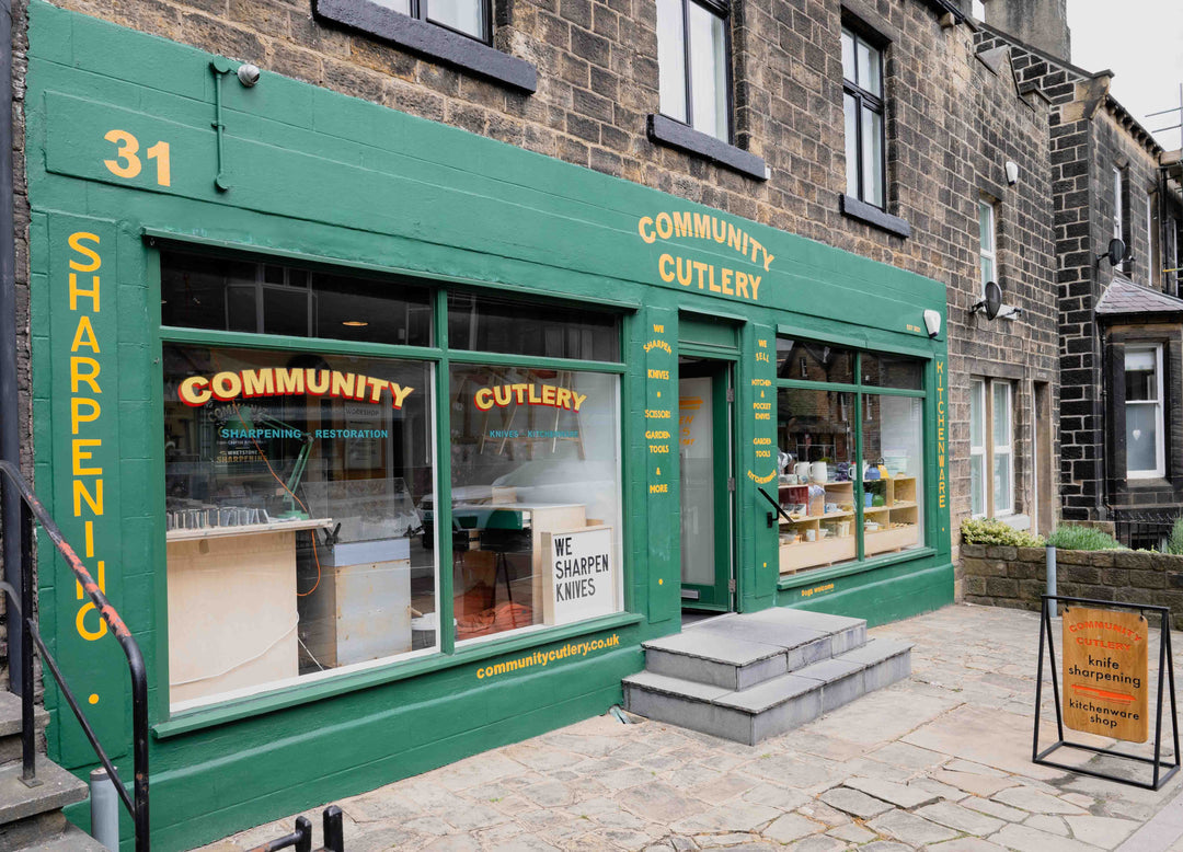 Green storefront with 'Community Cutlery' branding on a brick building.