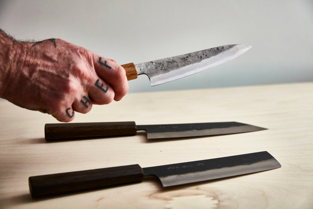 Mans hand with chef tattoo across knuckles holding a japanese kitchen knife