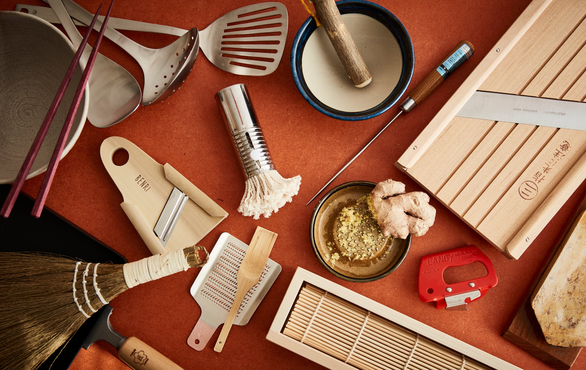 Large collection of Japanese kitchenware on orange background , including graters, mandolin, sushi maker, chopsticks and various utensils