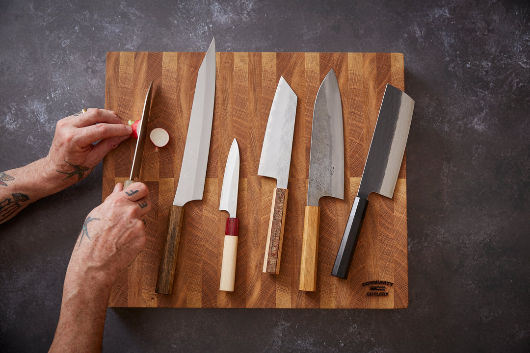 Collection of Japanese knives on a chopping board, one being used to halve a radish