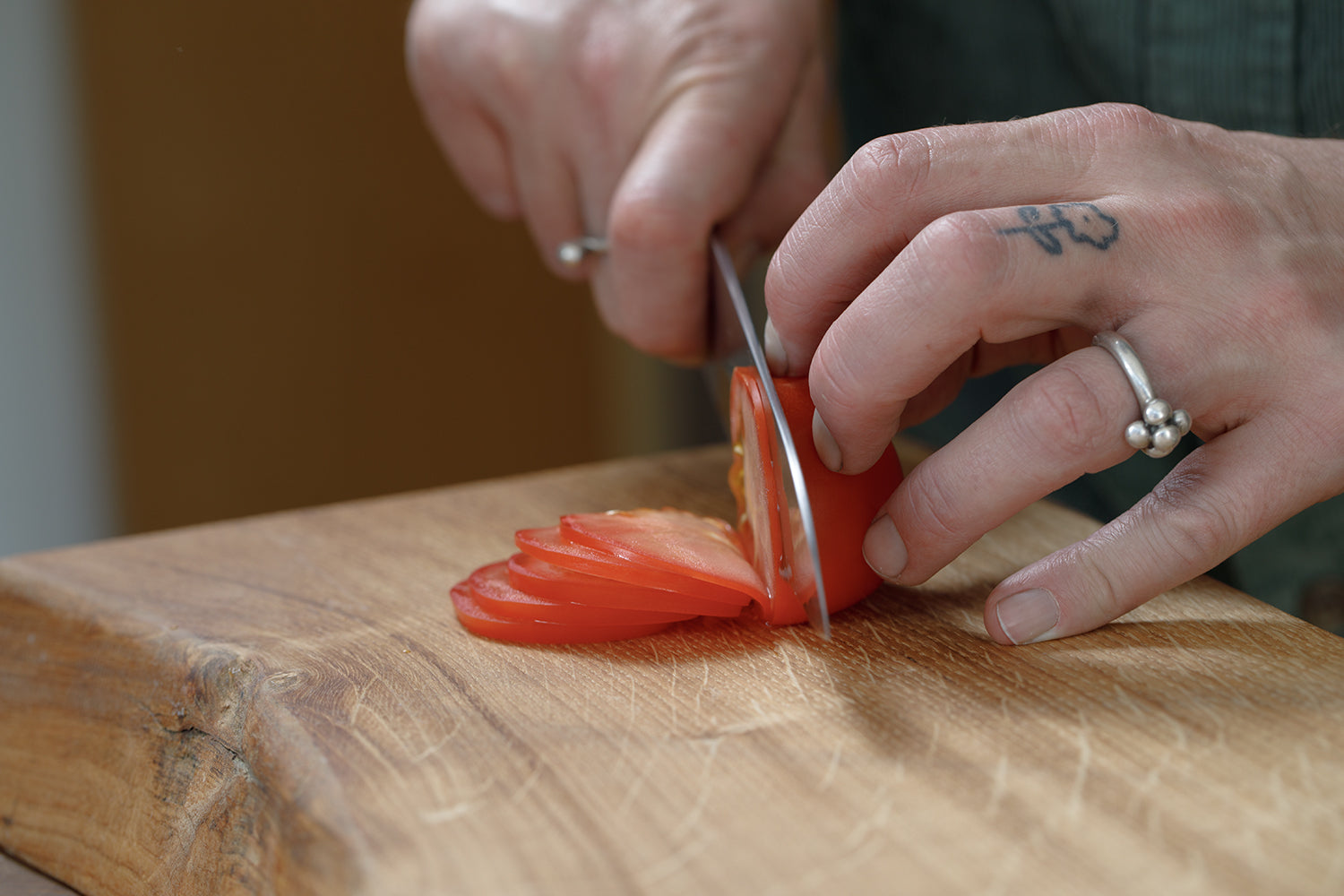 Person slicing a tomato on a wooden cutting board with a japanese kitchen knife