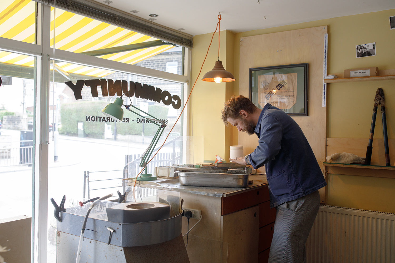 Person knife sharpening at a counter in a store with a yellow and white striped awning outside.