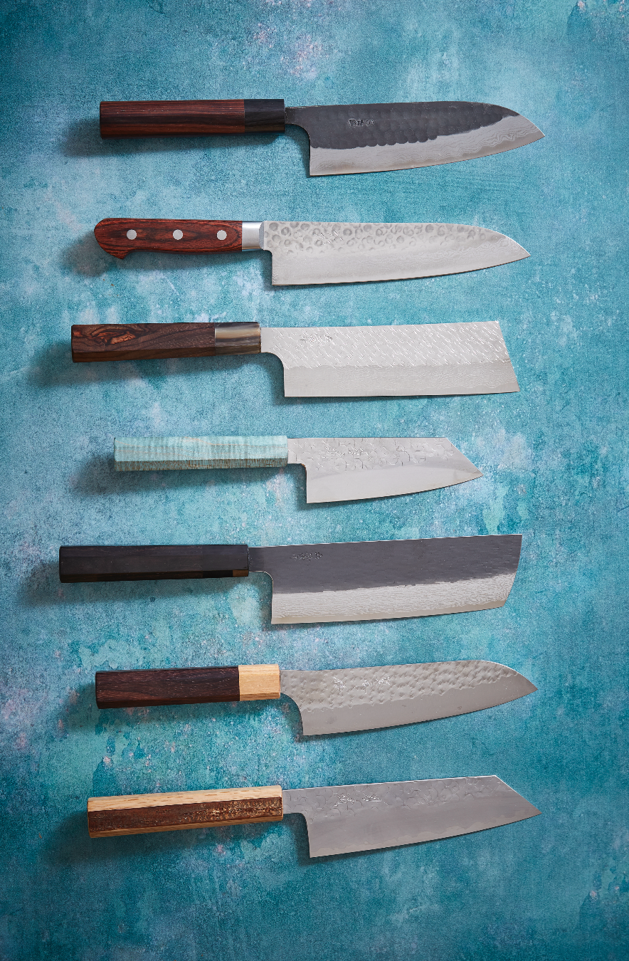 Seven handmade Japanese santoku kitchen knives on a blue background