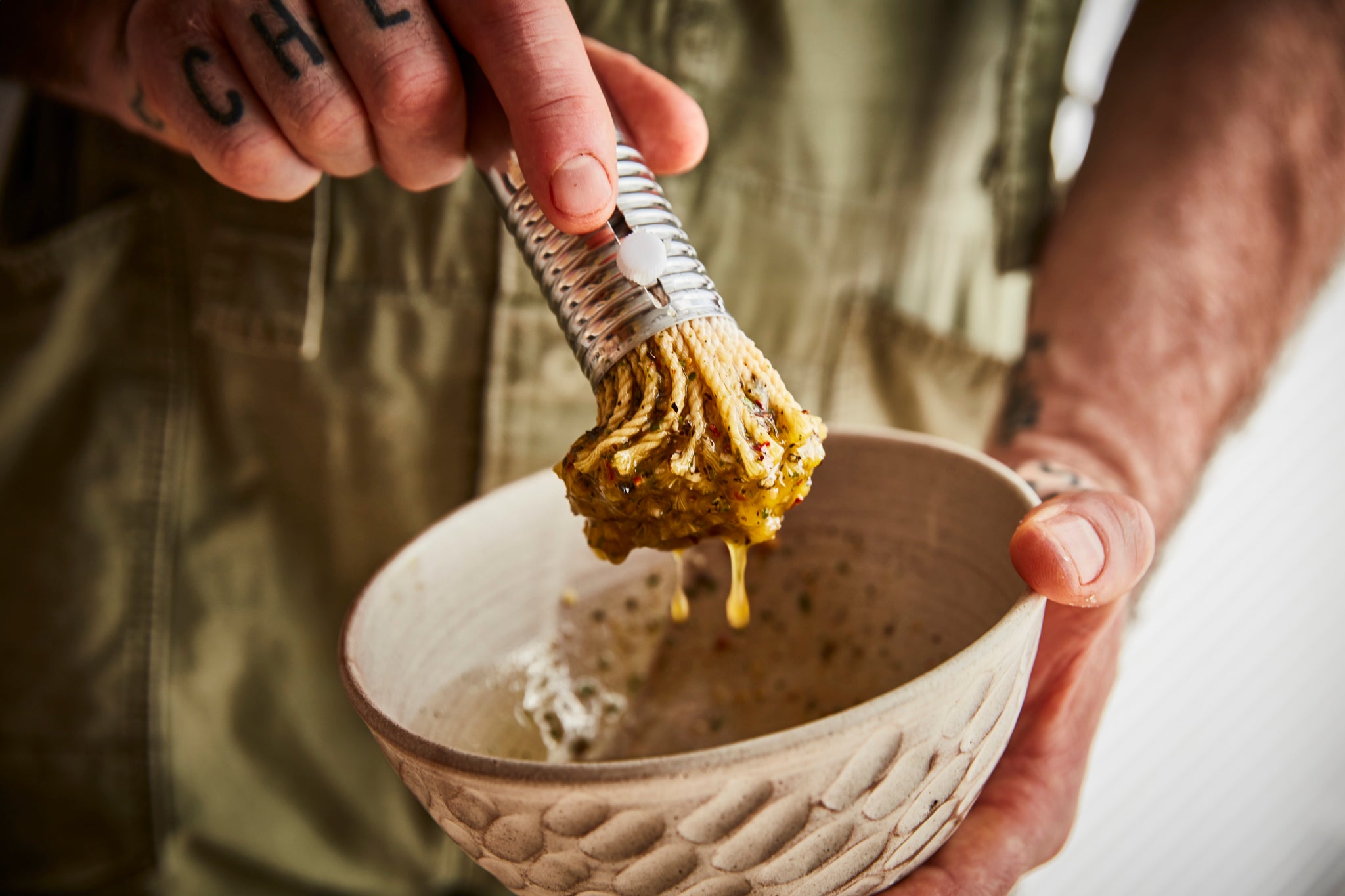 Male hands with chef tattoo on fingers - holding a bowl and dipping brush into marinade 